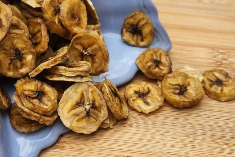 Dehydrated Banana Chips spilling out of a purple bowl onto a wooden table